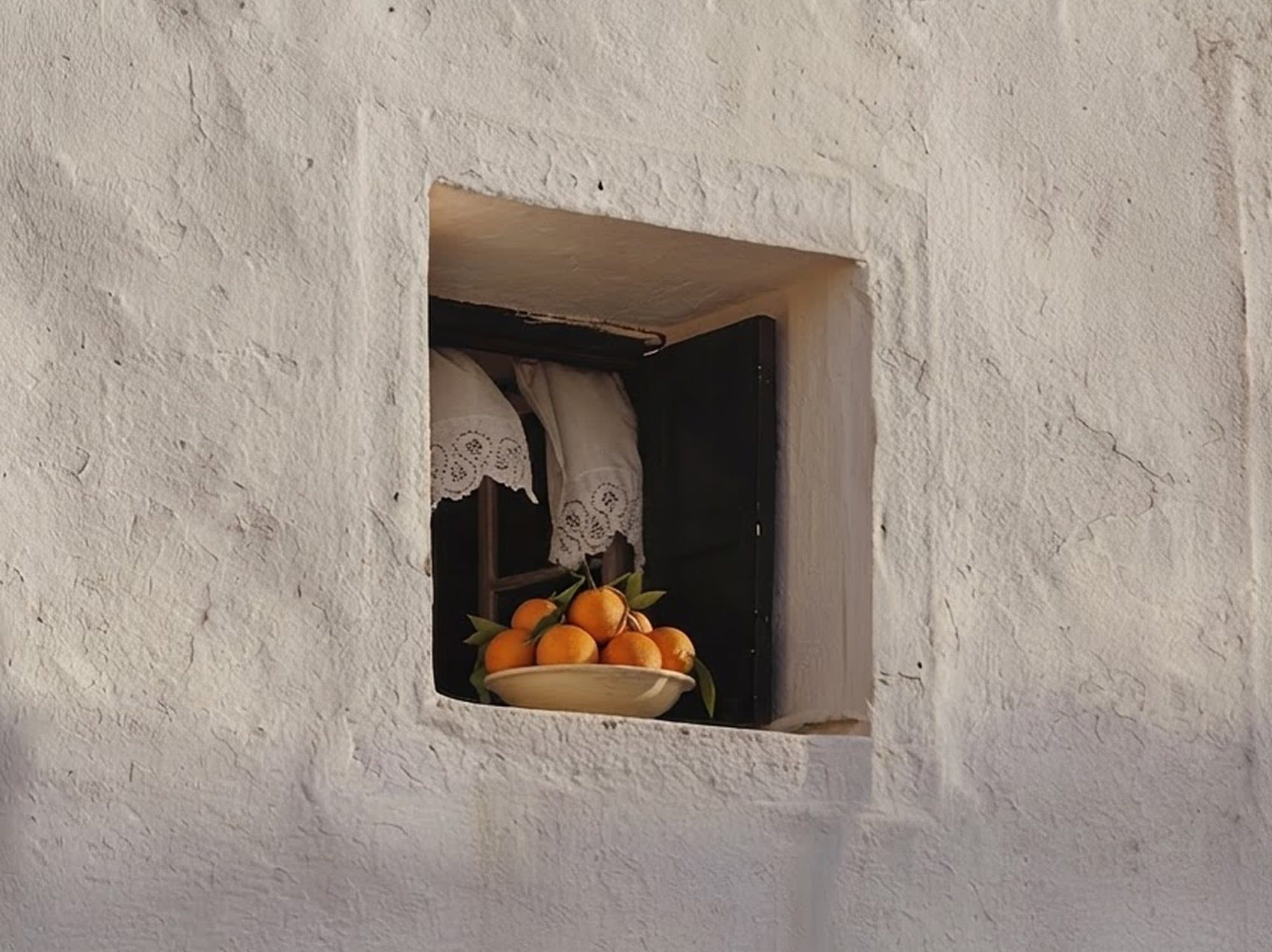 Ventana encalada con un plato de naranjas en el alféizar
